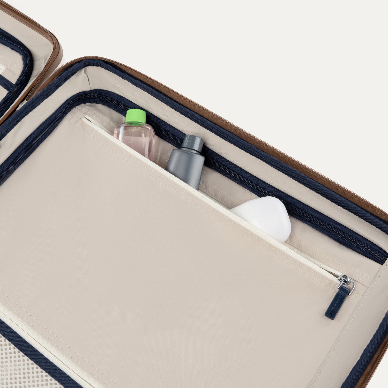 Open beige travel case with navy interior, containing toiletries on a white background
