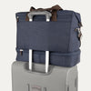 True navy weekender with brown handles and a navy rear strap over suitcase handle on a white background