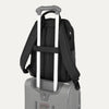 Black backpack with a rear strap over suitcase handle on a white background