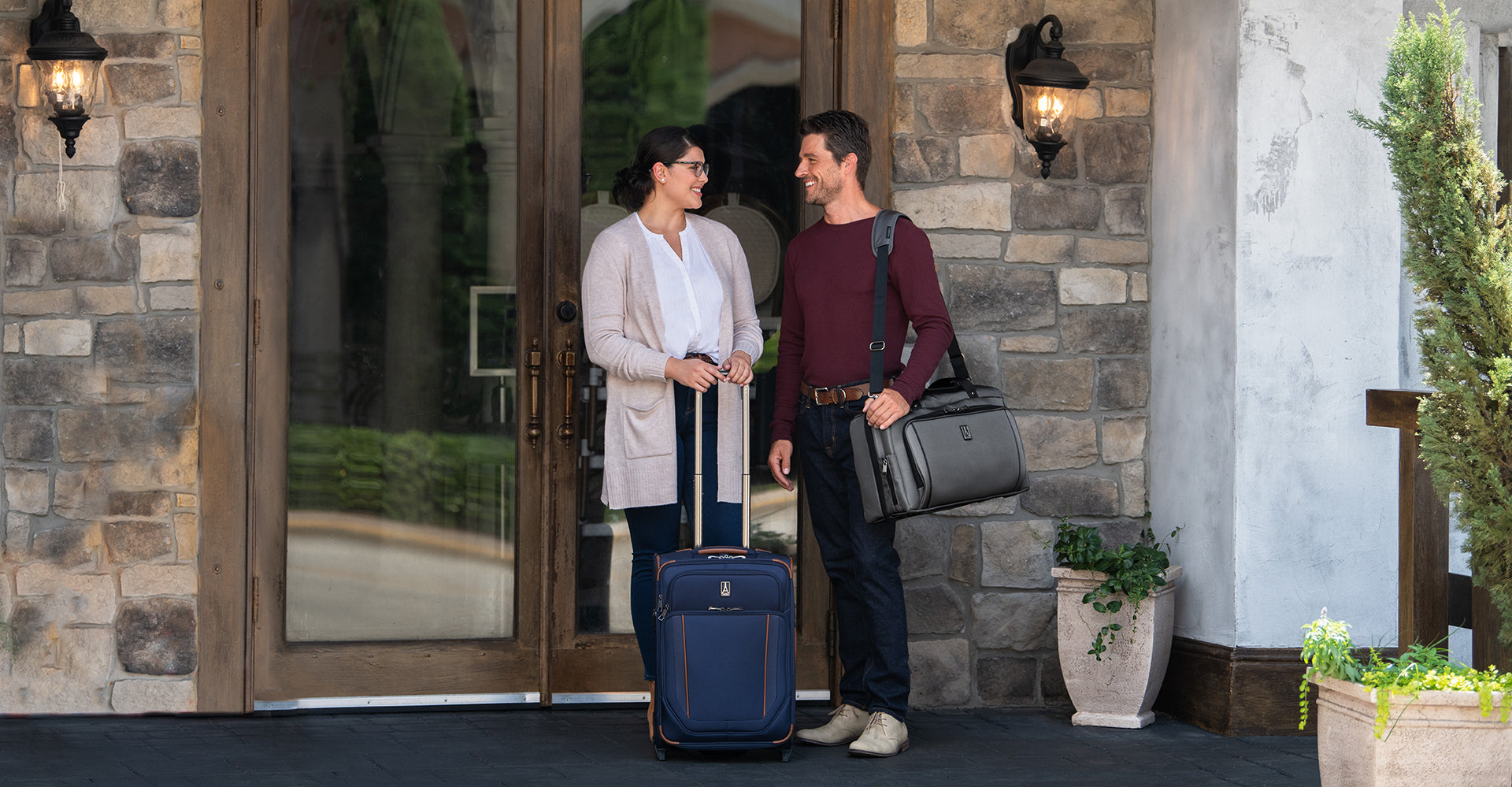 Man and woman carrying Travelpross duffel bag and rolling suitcase