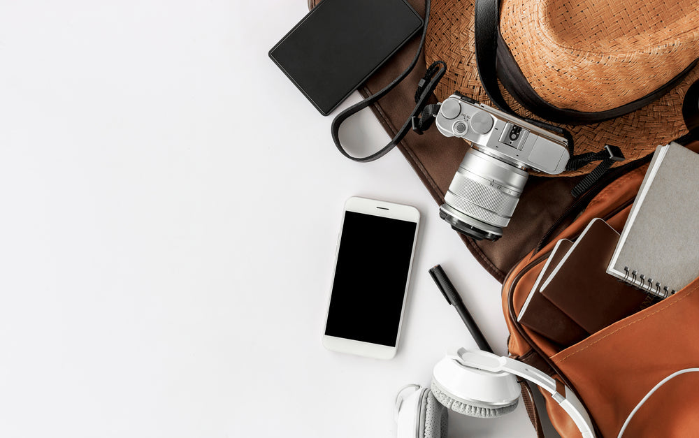 Phone, camera, headphones, wallet, notebook,pen, hat sitting on a table 