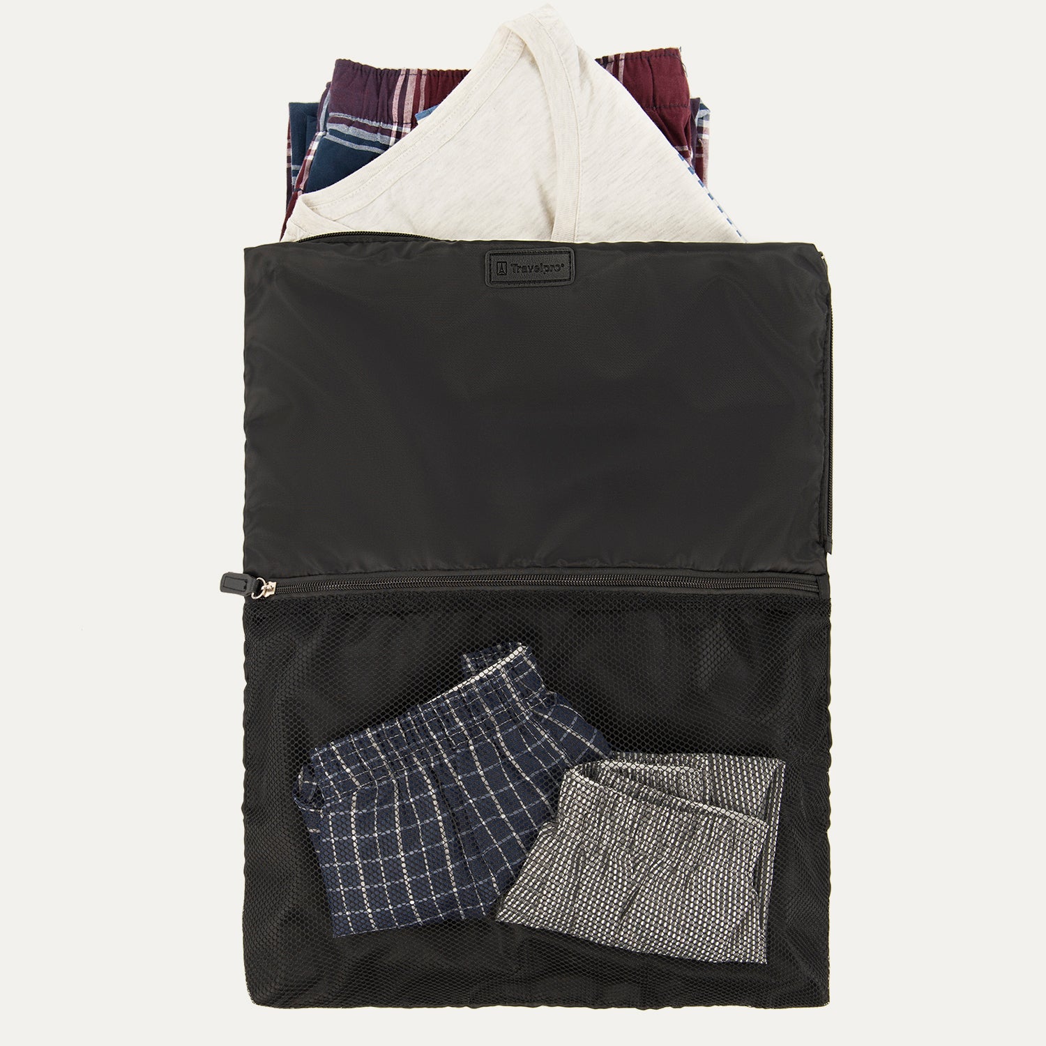 A black Travelpross Essentials washable laundry bag with a large zippered opening, displaying a white shirt and folded plaid and striped garments inside, alongside a mesh pocket with additional items.