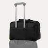 Black tote bag stacked on top of a piece of luggage with a light gray background