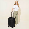 A person pulling a black carry-on spinner luggage with telescopic handle.