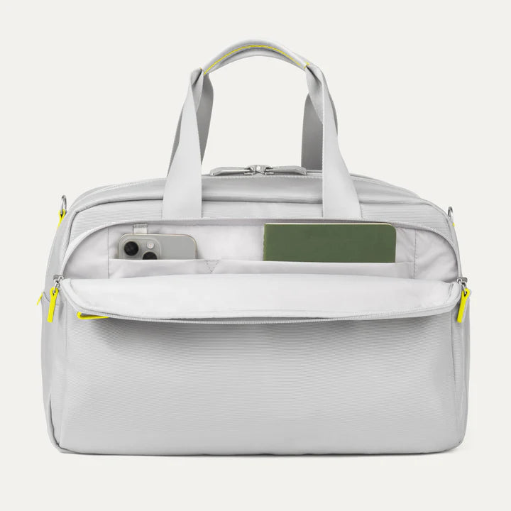 Front view of VersaPack®+ UnderSeat Tote in Cyber Lime, showing dual carry handles and an open exterior pocket with a phone and passport for easy access.