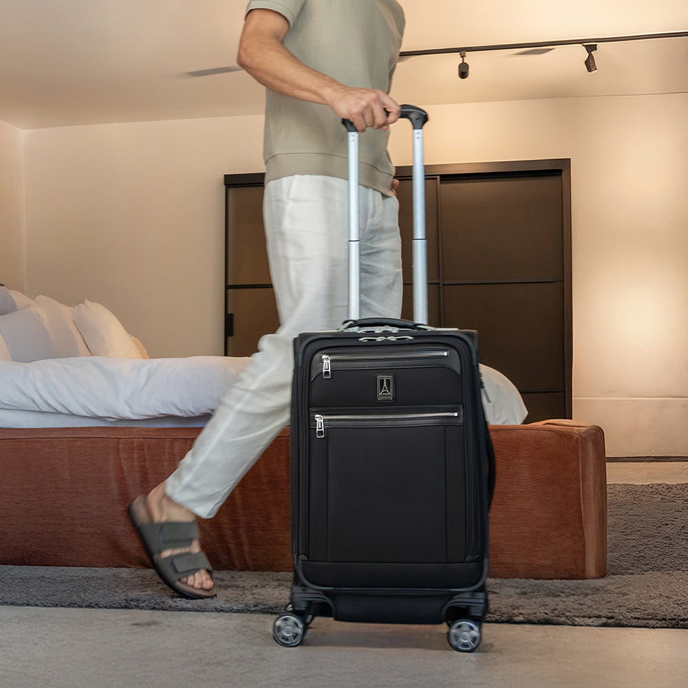 Person pulling a black suitcase in a hotel room.