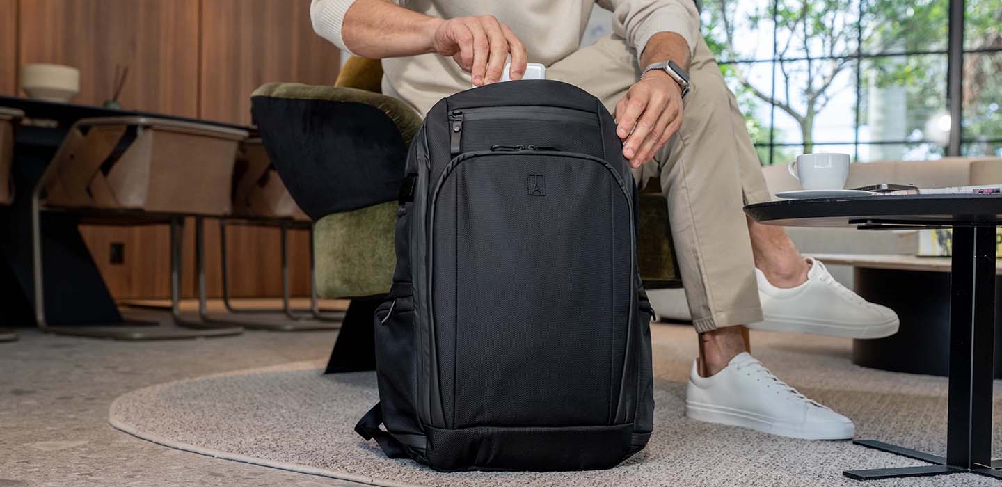 Person sitting on a chair with a black backpack in front of them in an indoor setting.