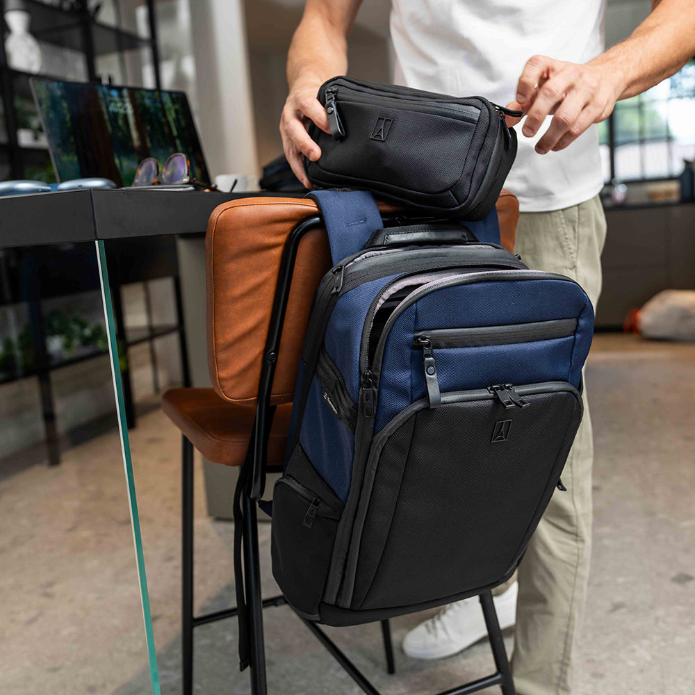 Person organizing a blue and black backpack with a small black bag on top, in an indoor setting.